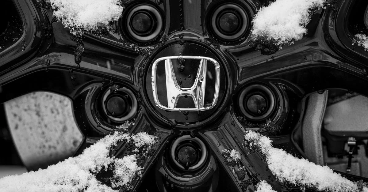 Gros plan en noir et blanc de l'emblème d'une roue Honda recouvert de neige, mettant en avant les conditions de conduite hivernales.
